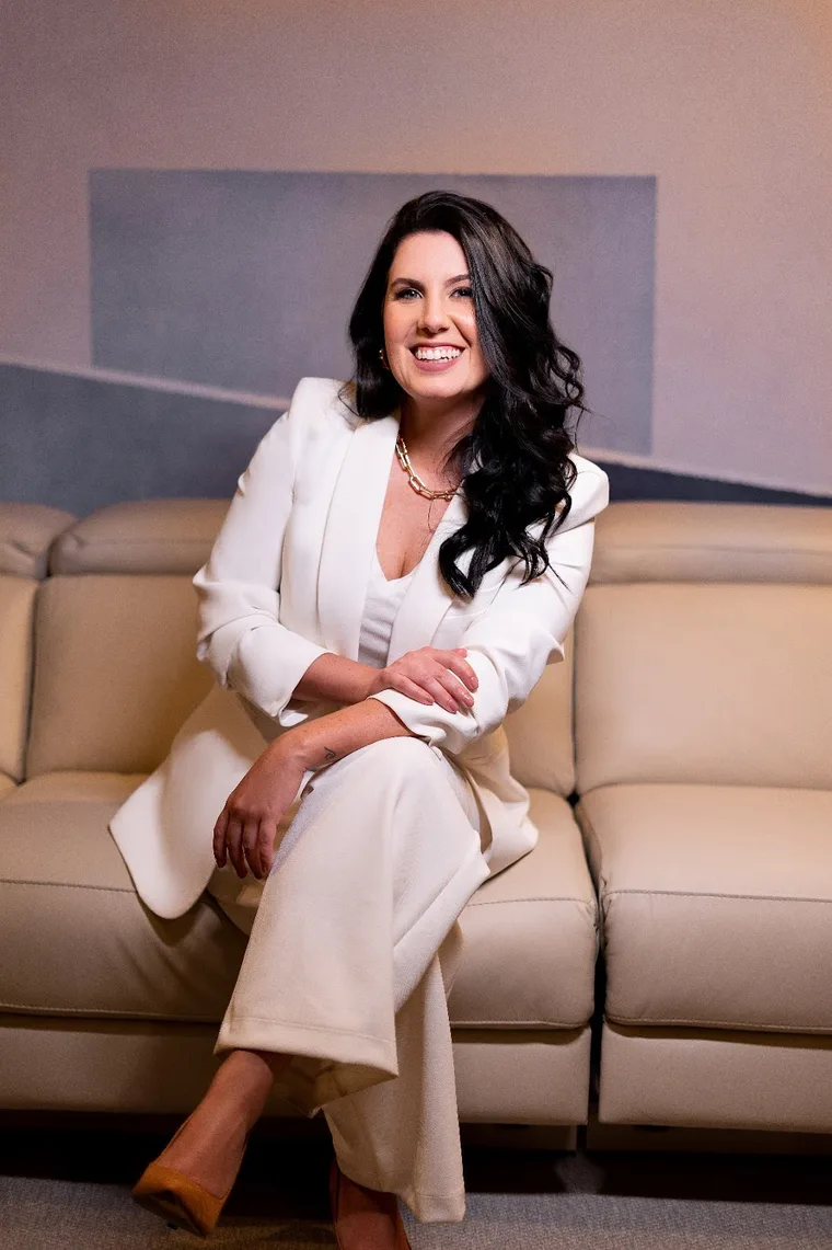 Dra. Maiara R. Frangiotti sorrindo, de terno claro, sentada num sofá