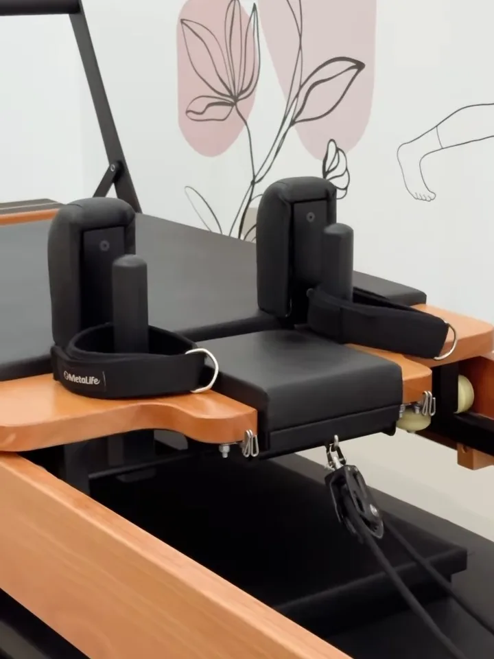 Aparelho de pilates com molas e alças, com uma ilustração na parede ao fundo