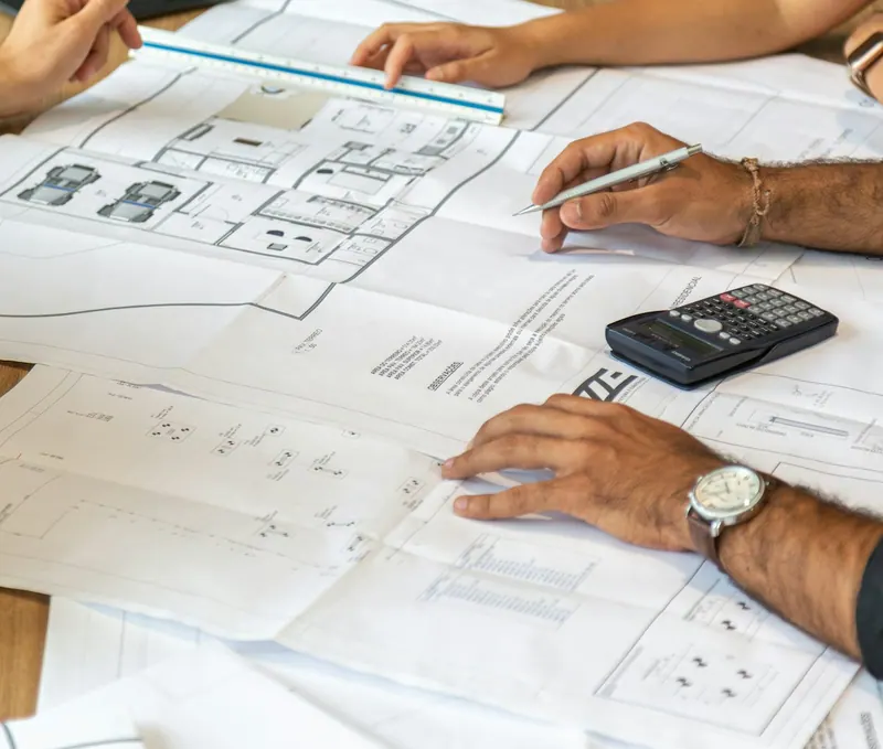 Mãos sobre plantas de arquitetura e uma calculadora